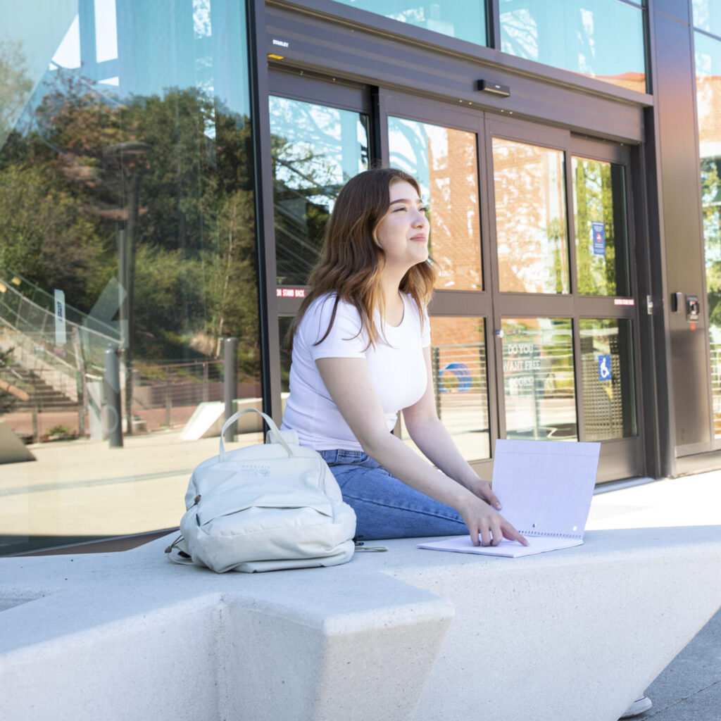 Female identifying student sitting on concrete sitting fixutre